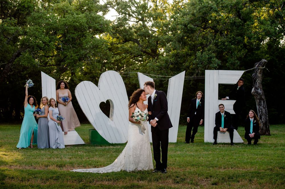 Wedding couple poses in front of large white LOVE letters outdoors.