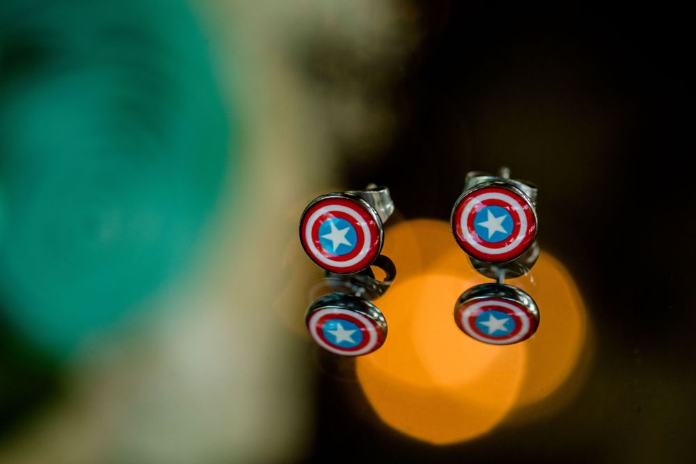 Captain America shield cufflinks displayed against a blurred orange and teal background.