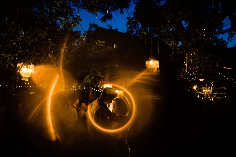 Light painting at night creates glowing circular patterns against a dark background with illuminated lanterns in trees.