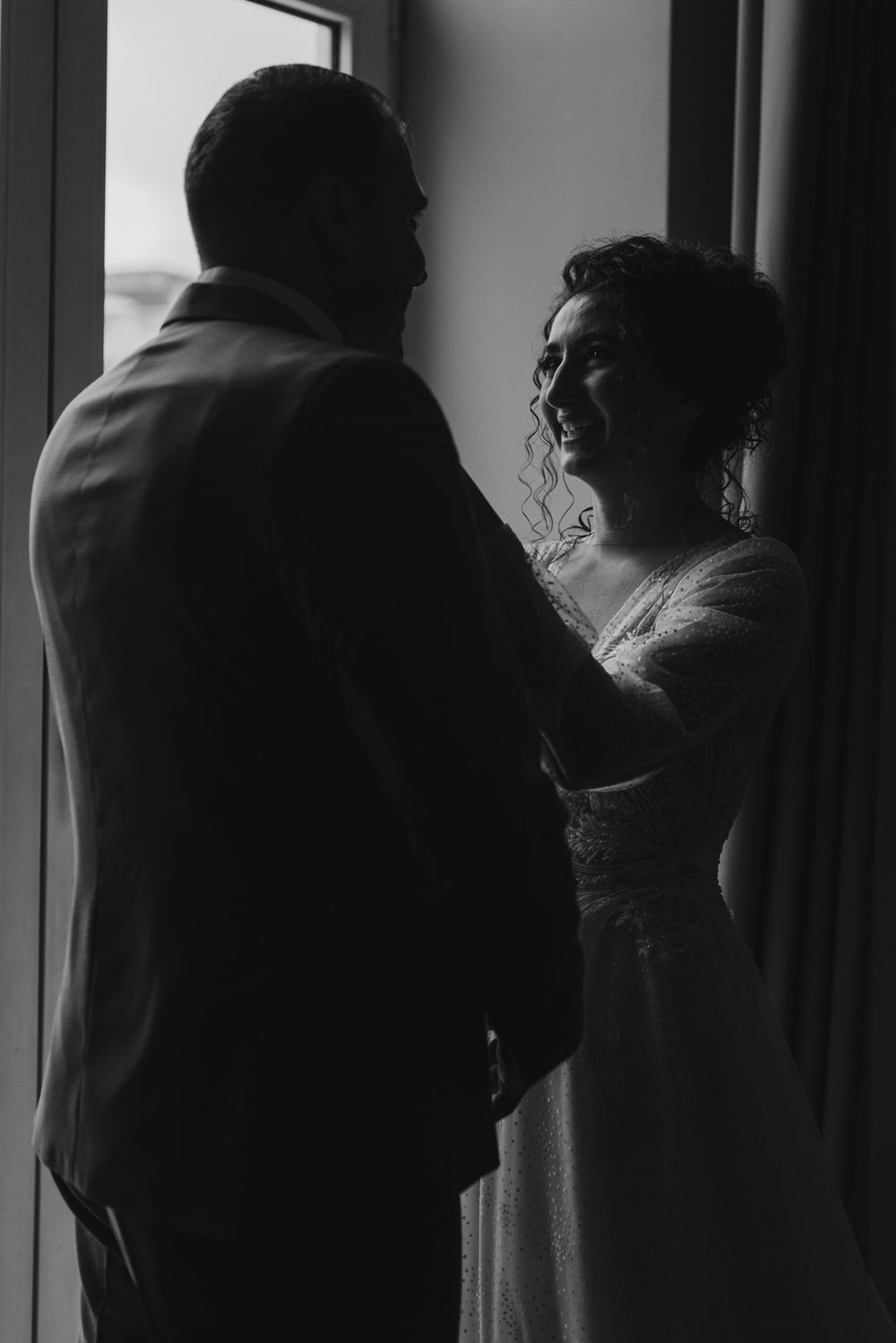 Silhouetted figures stand near window creating dramatic black and white wedding portrait.