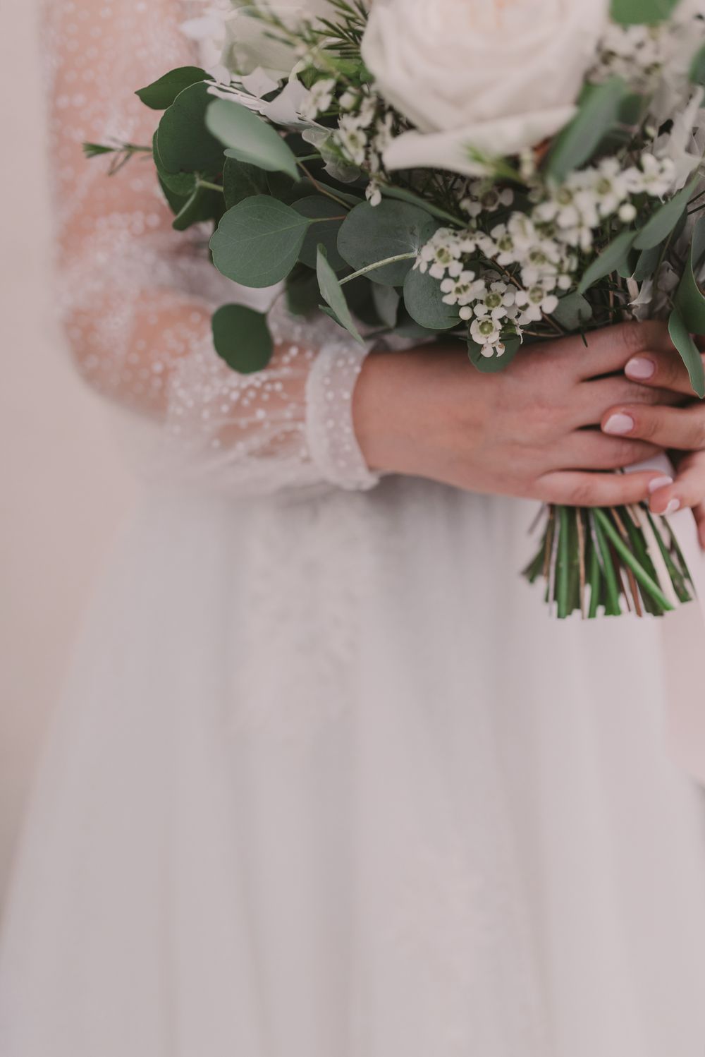 Wedding bouquet featuring white roses and eucalyptus leaves against a lace dress.