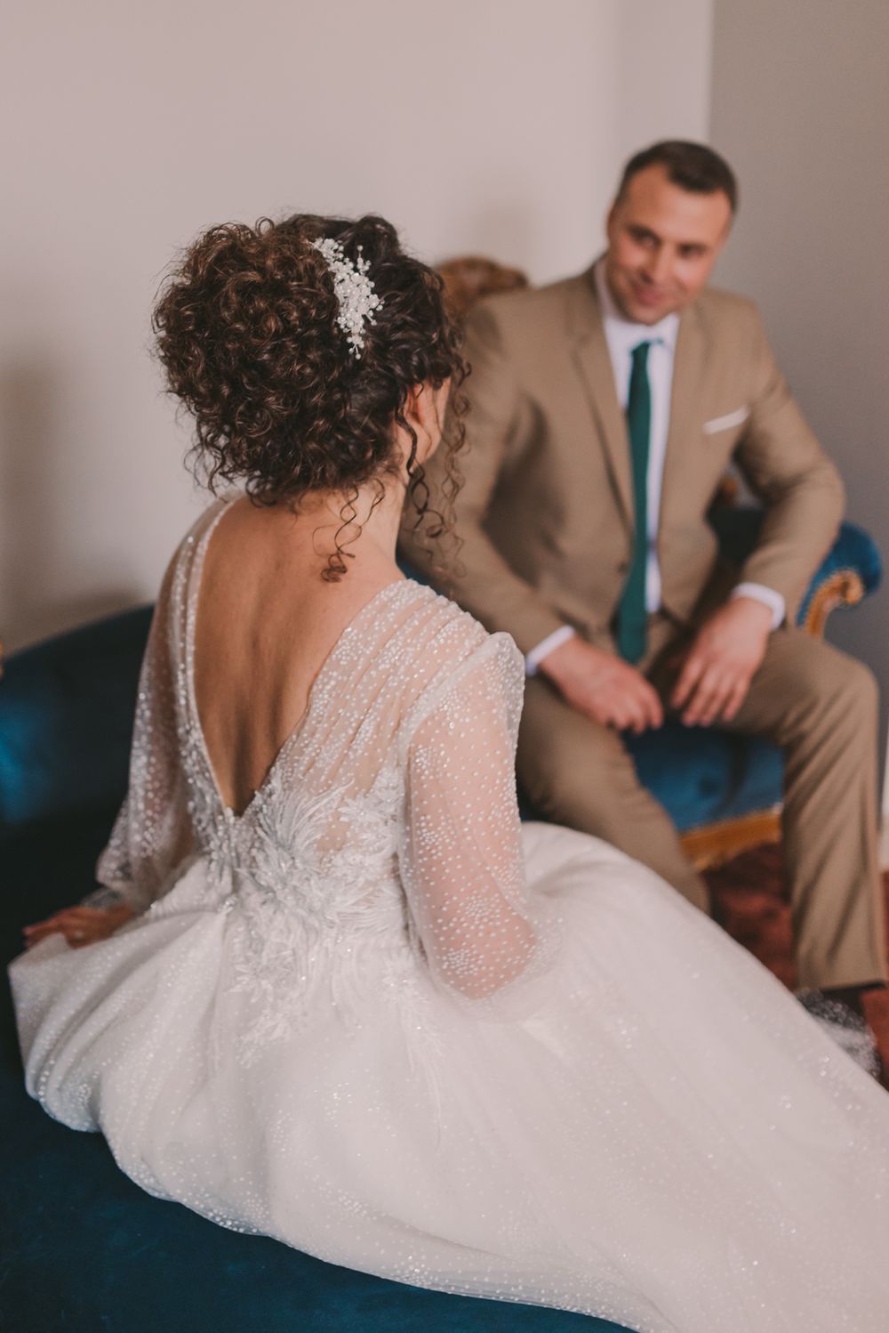 Bride in lace wedding gown reclines on blue velvet couch during formal portraits.