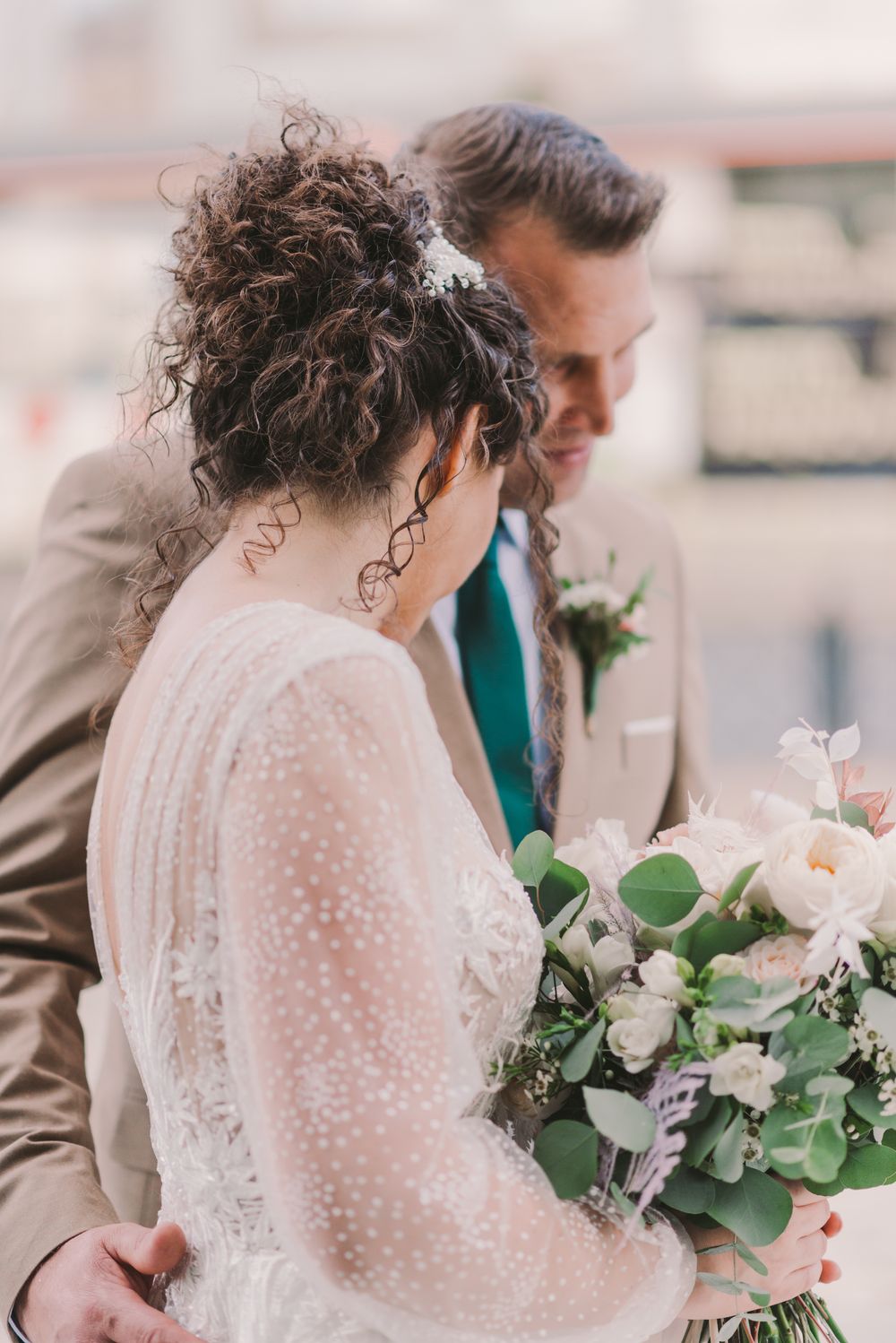 Elegant wedding dress with delicate lace details and a beautiful floral bouquet with greenery.