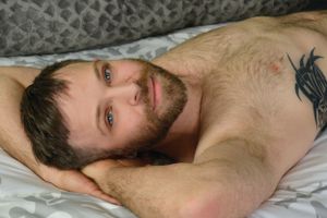 Artistic bedroom portrait showing relaxed pose and tattoo detail.