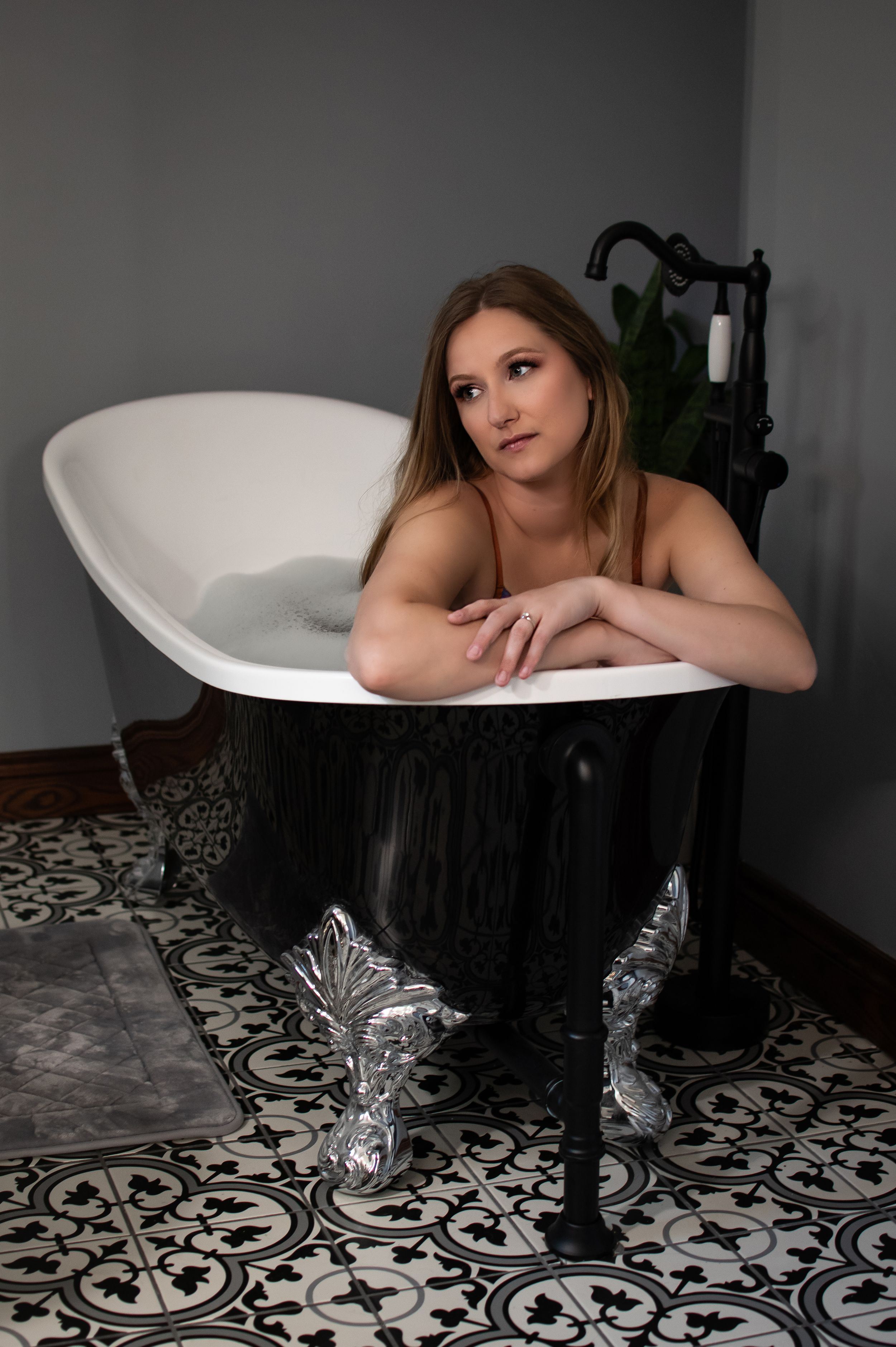Artistic boudoir photo featuring a vintage black and white clawfoot bathtub with decorative tile floor.