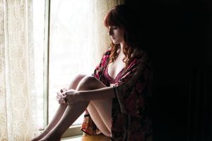 Silhouetted figure in floral robe sitting by window in moody lighting.