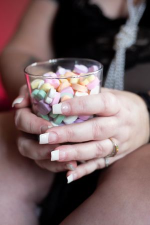 Close-up of manicured hands holding glass of colorful marshmallows.