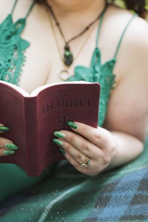 Close-up of hands holding The Hobbit book while wearing green fantasy-inspired costume and jewelry.
