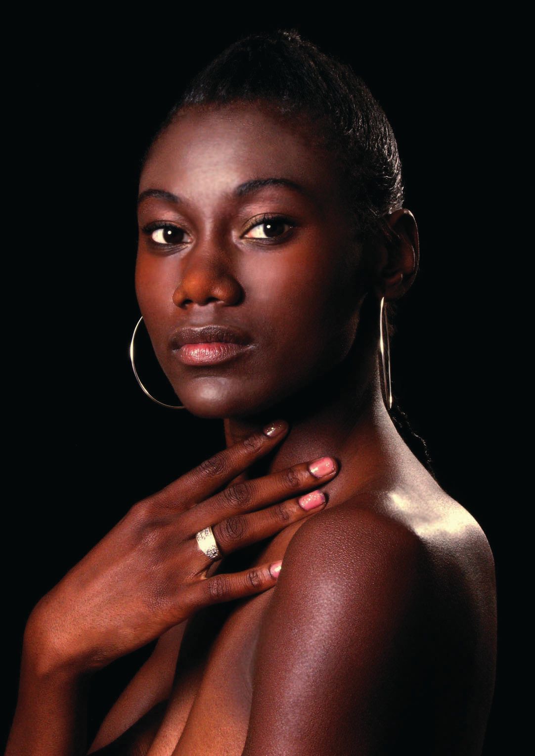 Dramatic beauty portrait with gold hoop earrings against dark background.