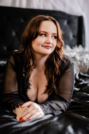Person in sheer black lace on dark leather couch with soft lighting.