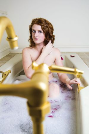 Artistic bathtub portrait with gold fixtures and bubble bath.