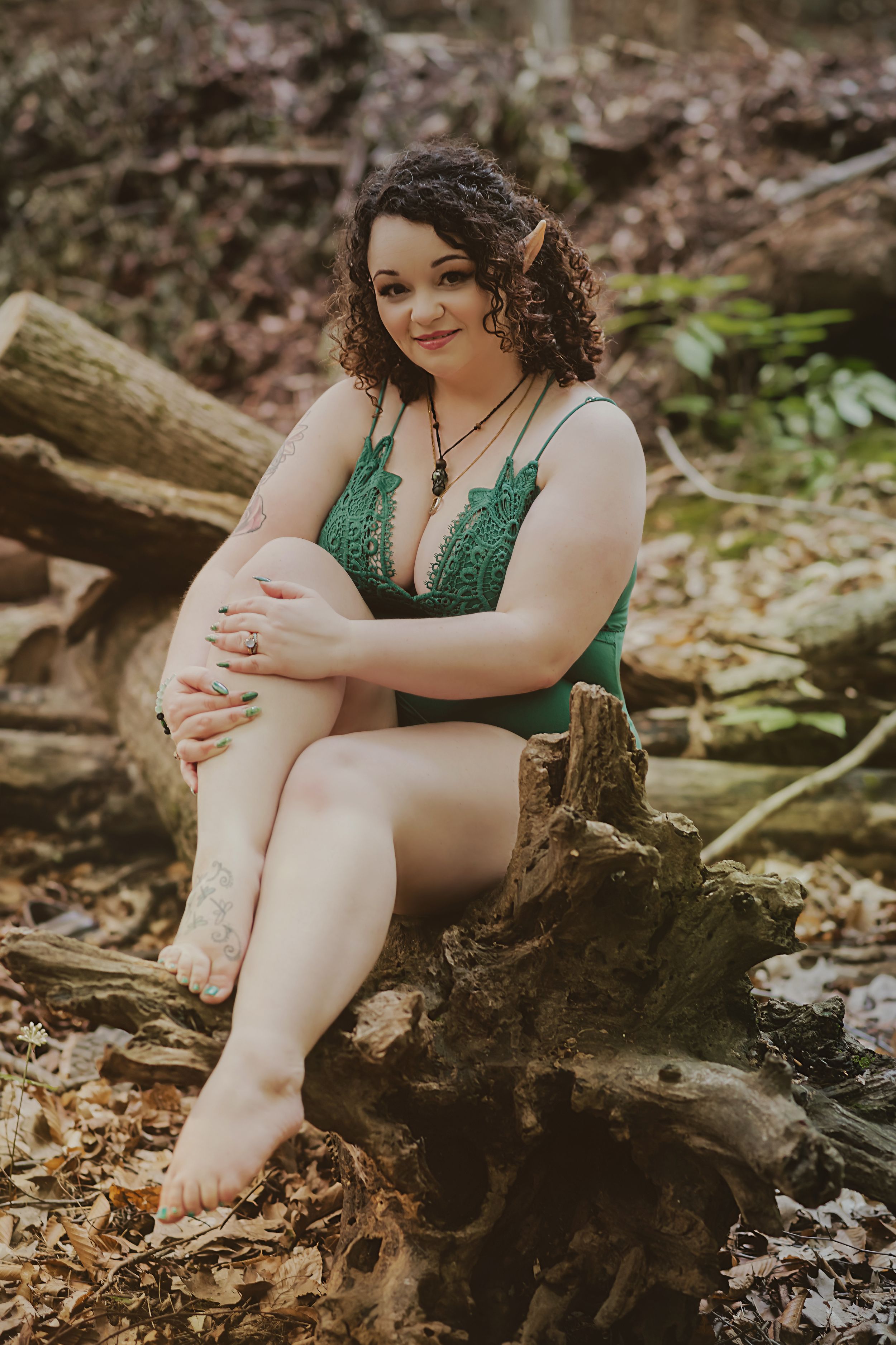 Forest photoshoot with emerald green attire sitting on fallen log.