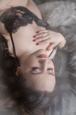 Artistic boudoir portrait with black lace on soft gray fur backdrop.