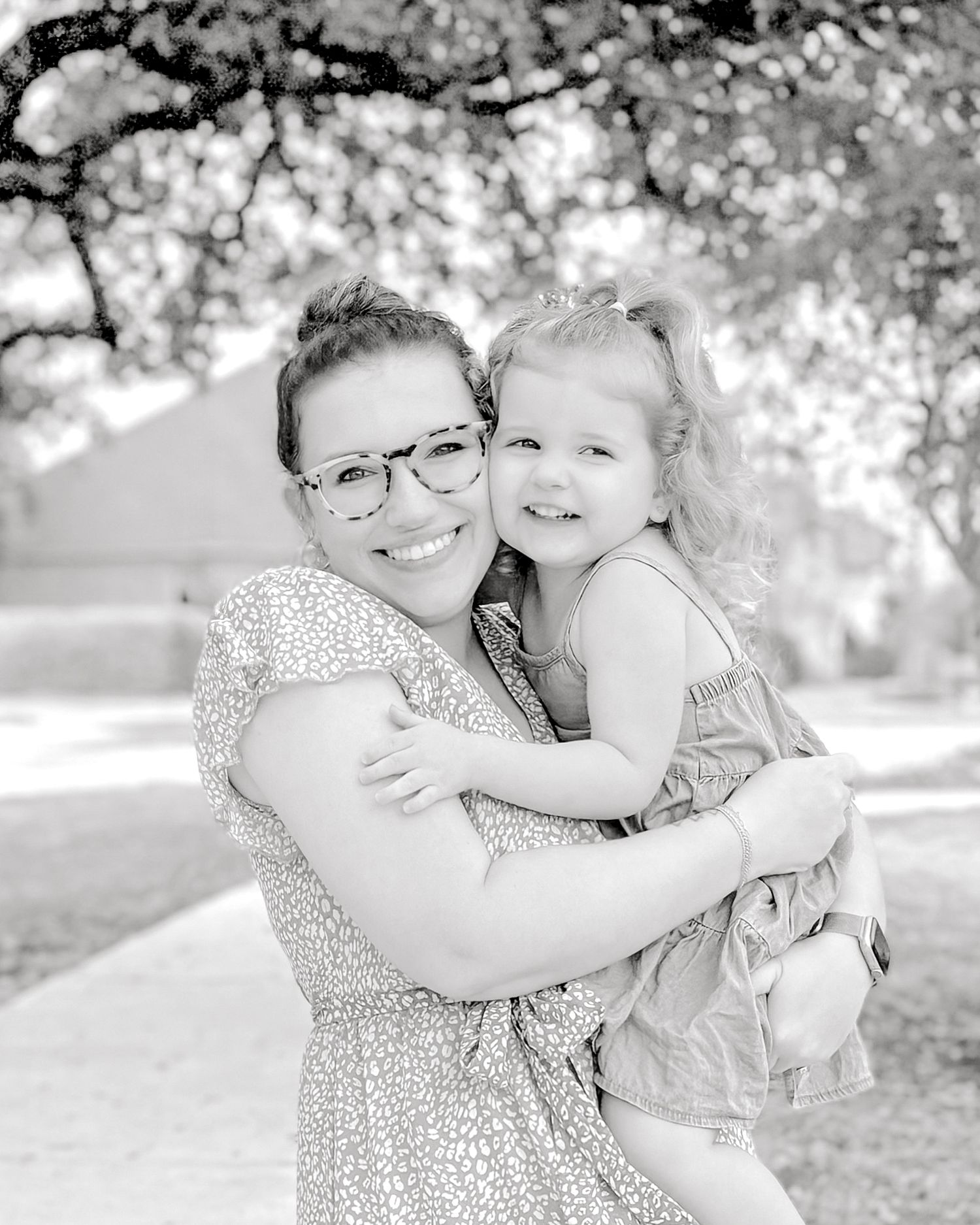 Black and white portrait of two people embracing outdoors under blooming trees.