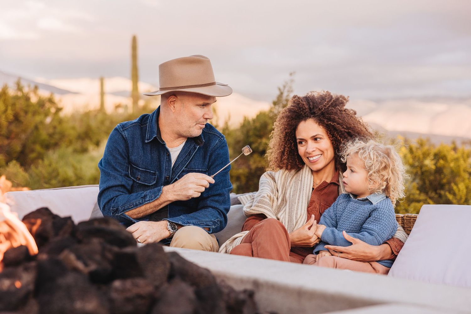 Family enjoying conversation around outdoor fire pit in desert setting.