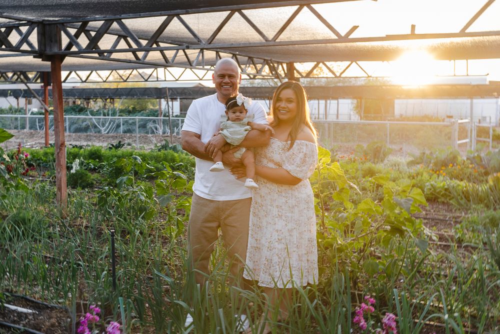 A family poses together at sunset under an outdoor structure with flowers in the foreground.