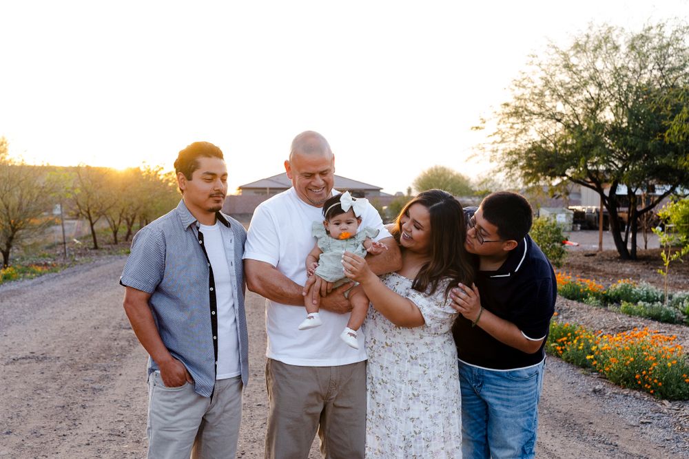 A group shares laughter while holding a baby outdoors during golden hour.
