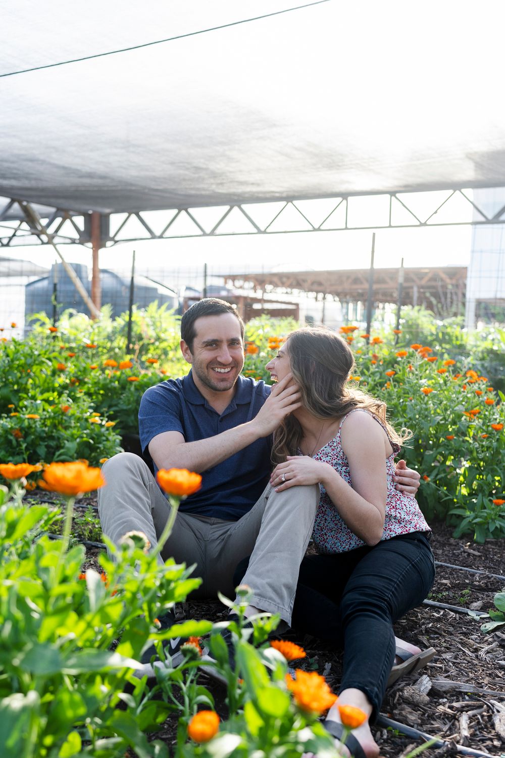 Couple sharing tender moment among blooming marigolds under greenhouse covering.
