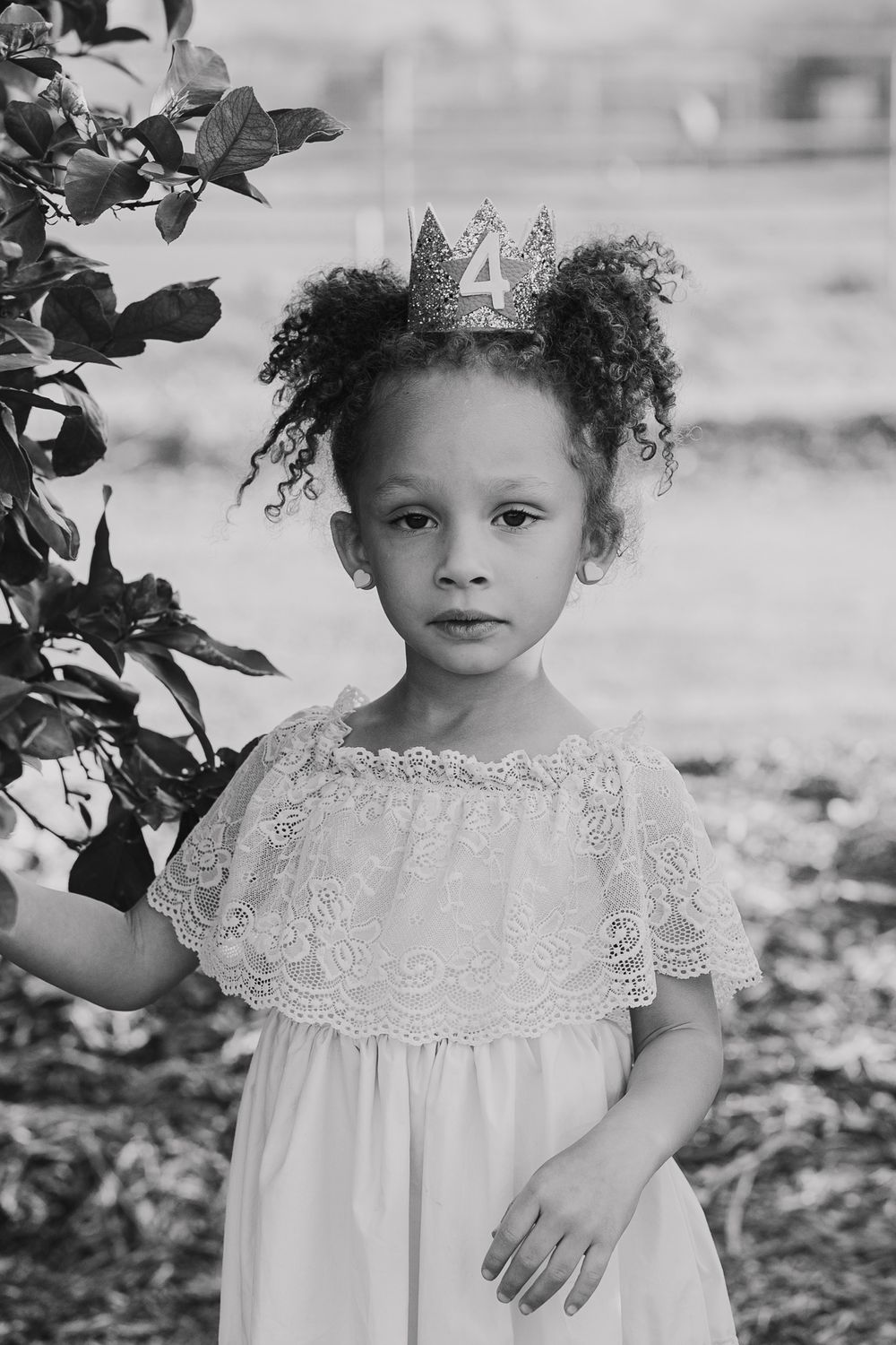 Young child wearing lace dress and crown with natural curly hair in black and white portrait.