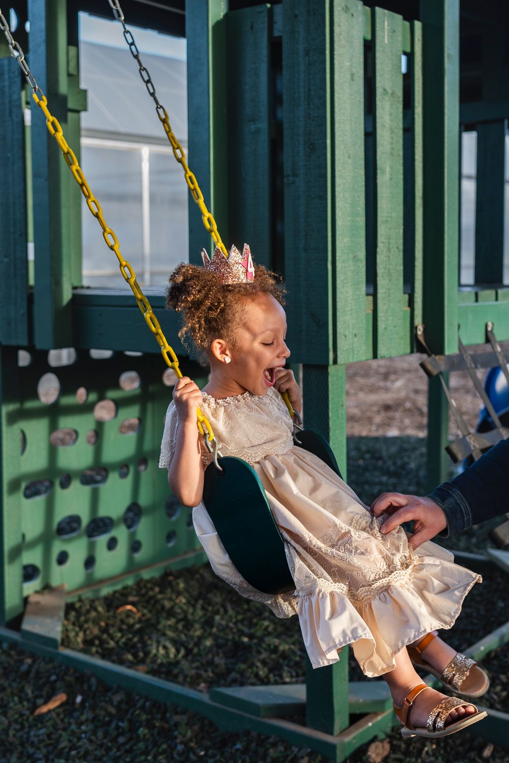 A joyful moment captured on a playground swing set while wearing a princess dress and crown.