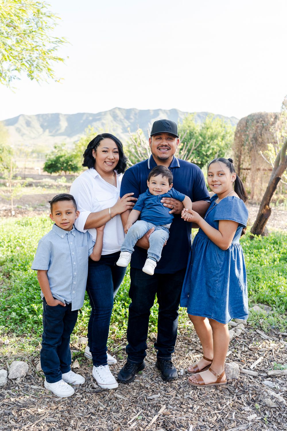 A happy family poses together for a portrait with mountains and greenery in the background.