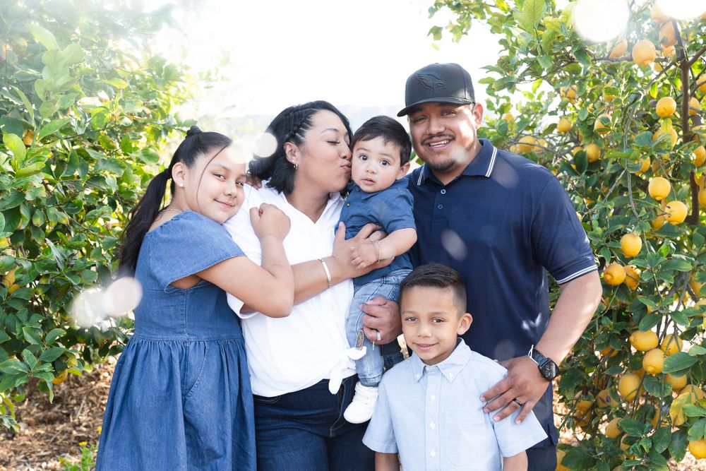Happy family portrait in a citrus grove with orange trees in the background.
