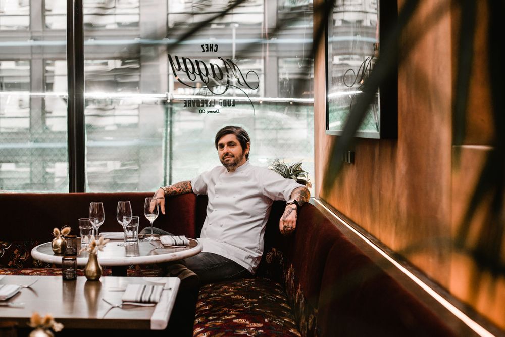 Chef sitting alone in elegant restaurant booth by window at night.