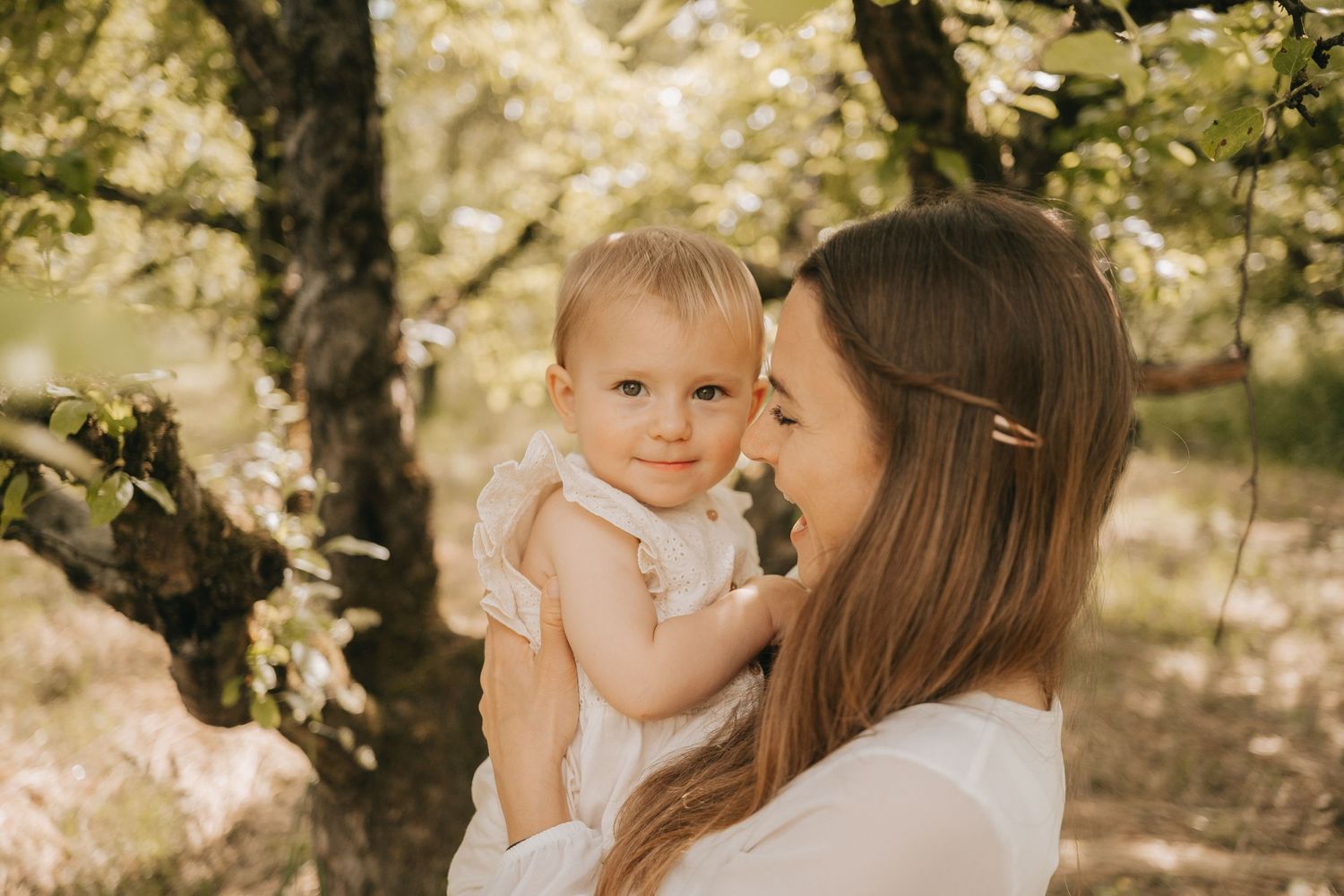 Tender moment between mother and baby in soft natural lighting under a tree.