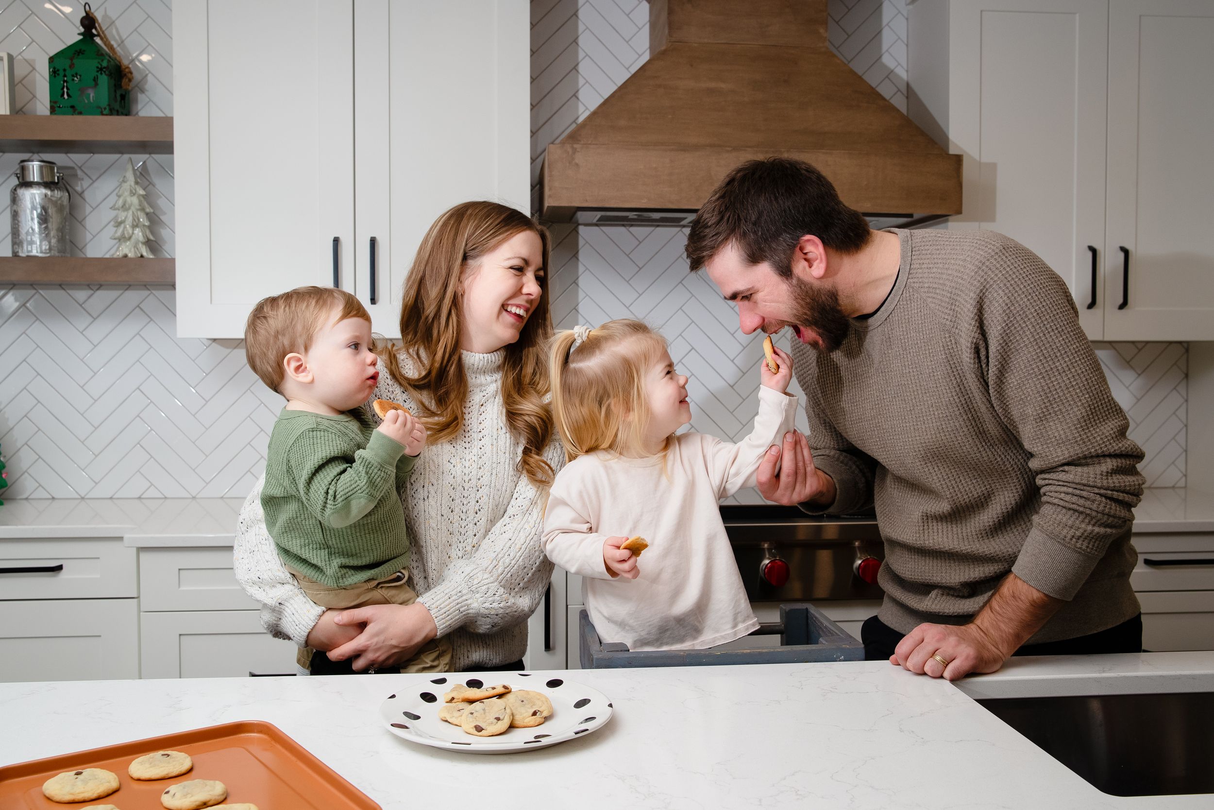 A joyful family moment gathered around a plate of cookies in a modern white kitchen.