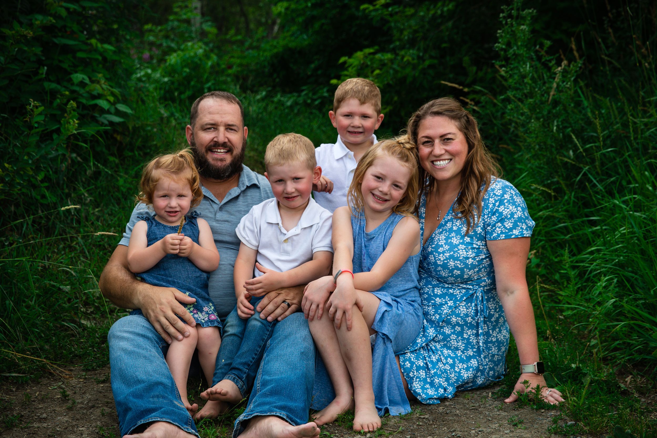 Family sitting together outdoors on a nature trail surrounded by lush greenery.