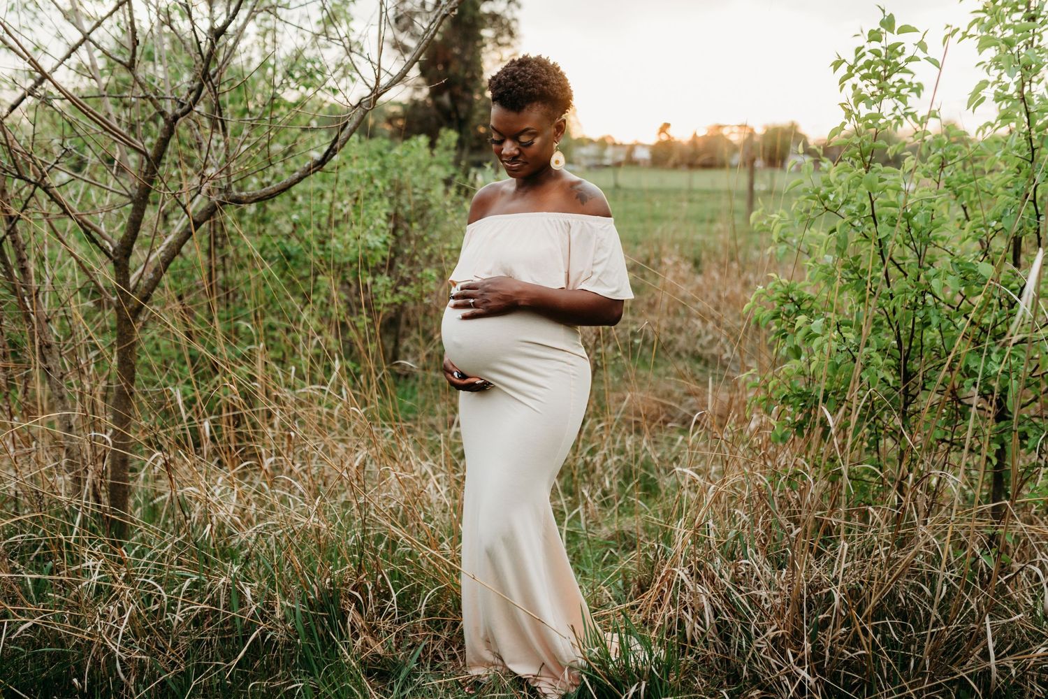 Pregnant mother stands looking at her belly while at Overlook Park near sunset