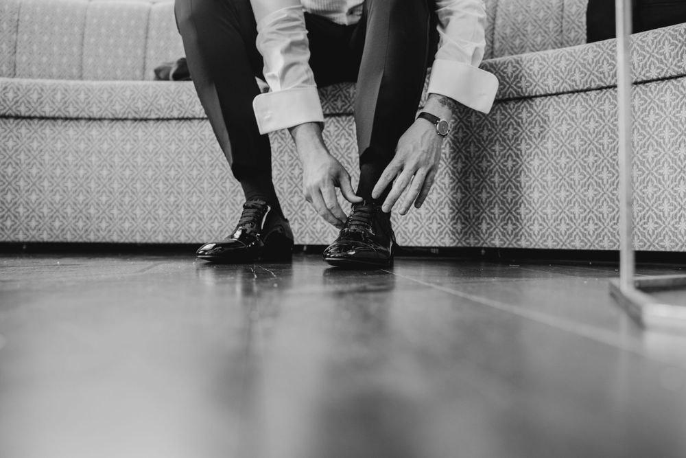 Close-up shot of person tying formal dress shoes on hardwood floor.