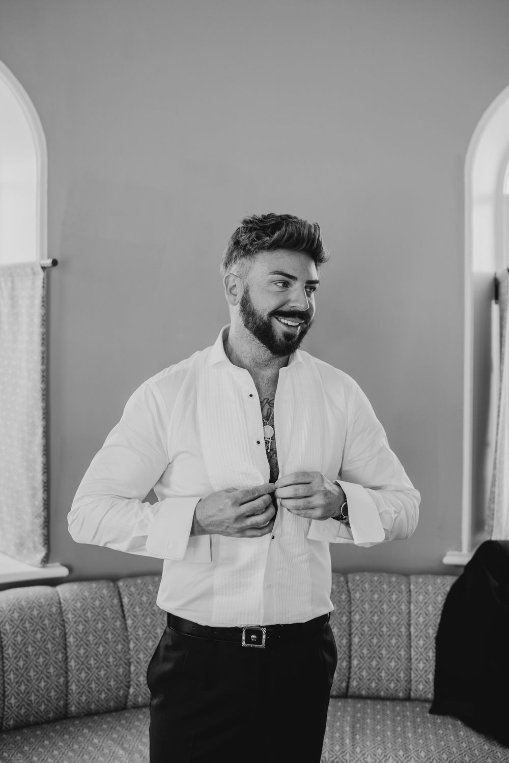 Groom adjusting white tuxedo jacket in formal preparation room.
