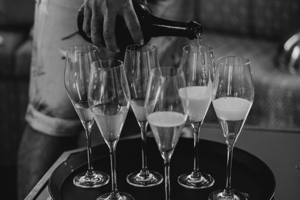Champagne being poured into multiple flute glasses on dark serving tray.