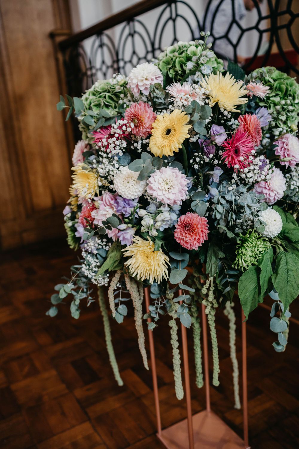 Colorful wedding flower arrangement featuring gerberas and hydrangeas on metal stand.