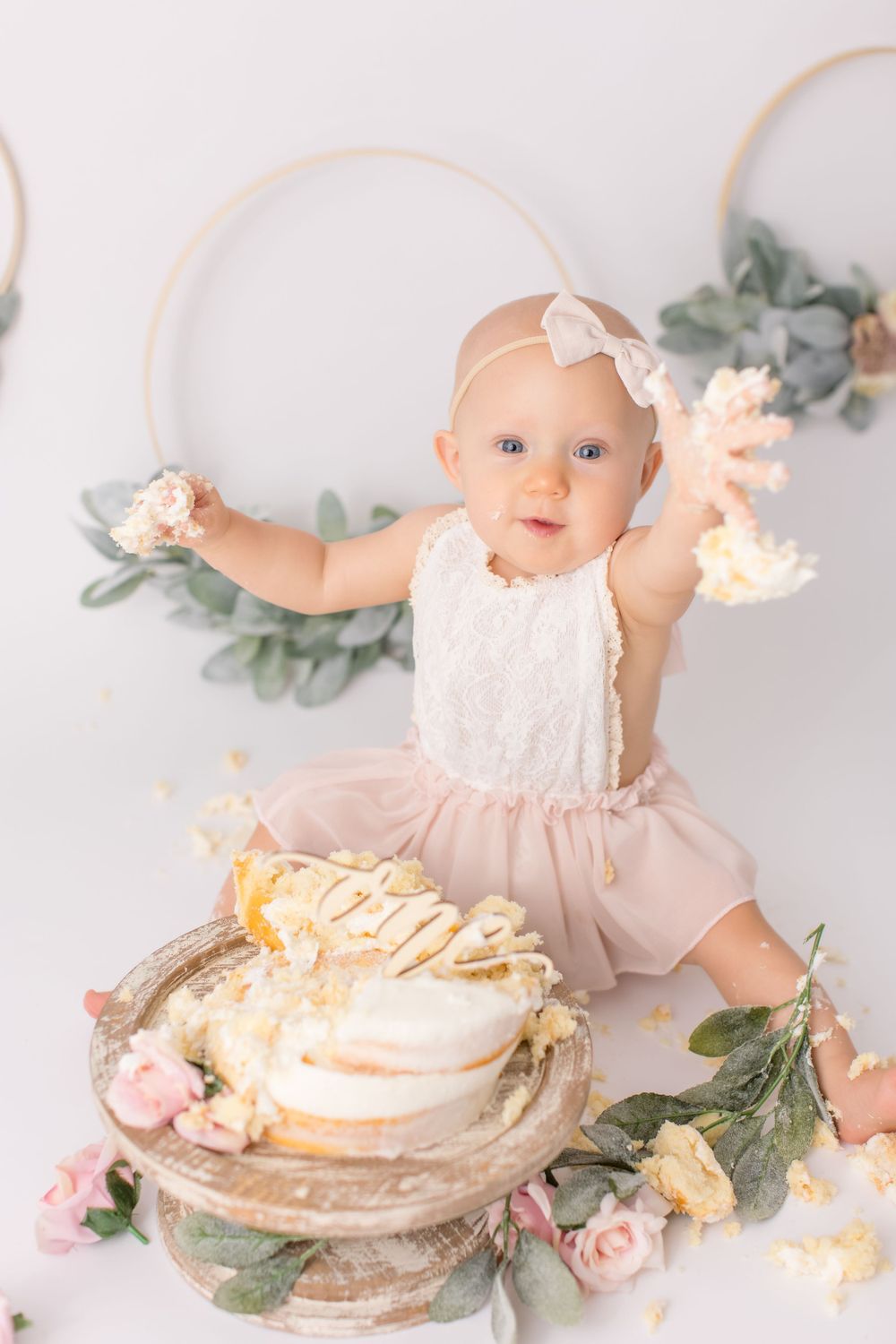Baby playing with cake during cake smash photoshoot with floral decorations.