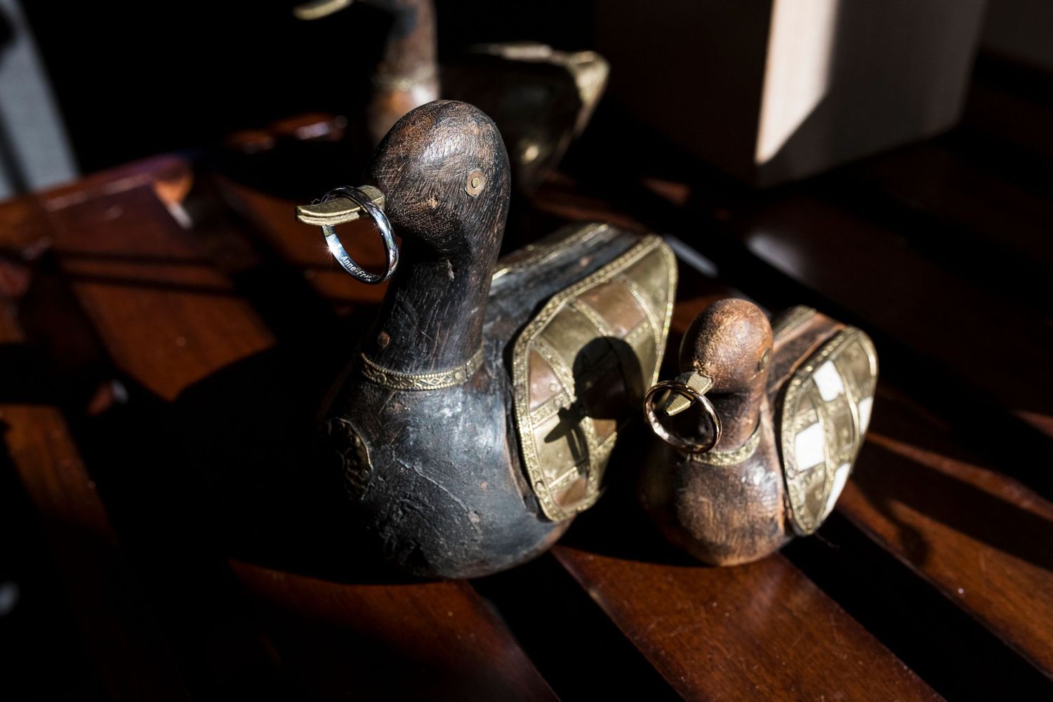 Vintage duck-shaped brass bells sitting on dark wooden surface.