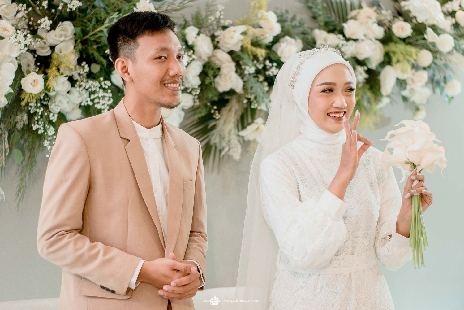 A candid wedding moment showing the couple laughing against a beautiful floral backdrop.