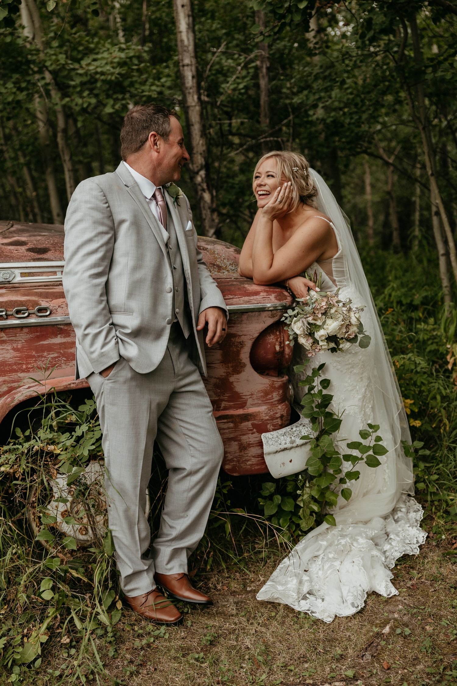 A romantic wedding moment shared by a couple next to a rustic red truck in a wooded setting.