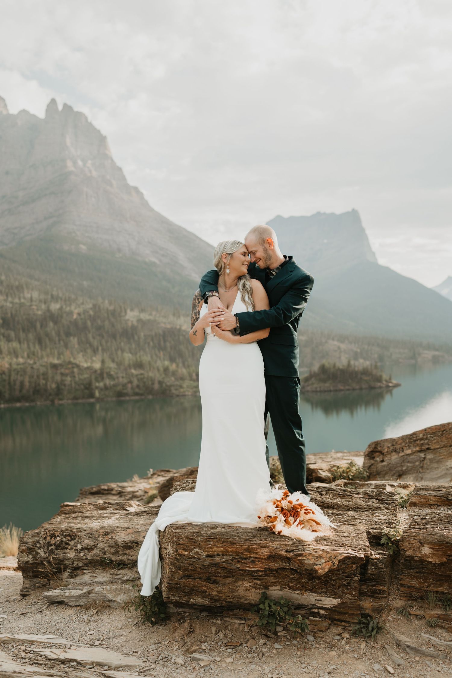 Wedding couple embracing on rocky overlook above mountain lake.