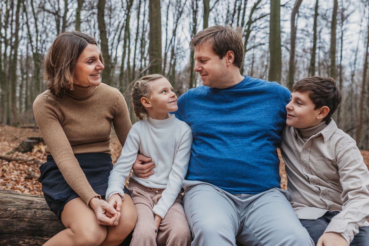 Family enjoying casual moment together while sitting on fallen log in forest.