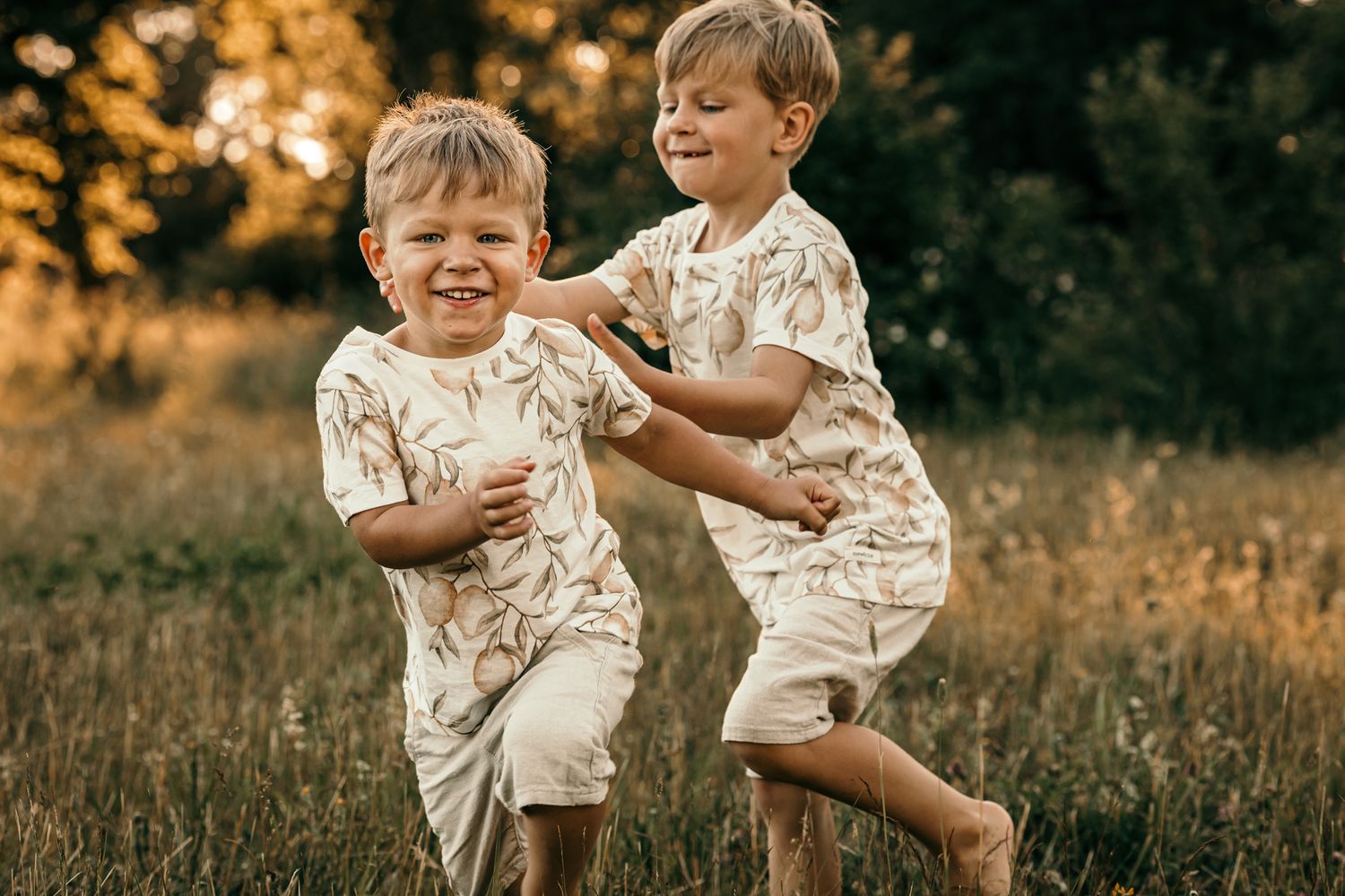 Två syskon springer barfota omkring på en äng och leker vid en familjefotografering.