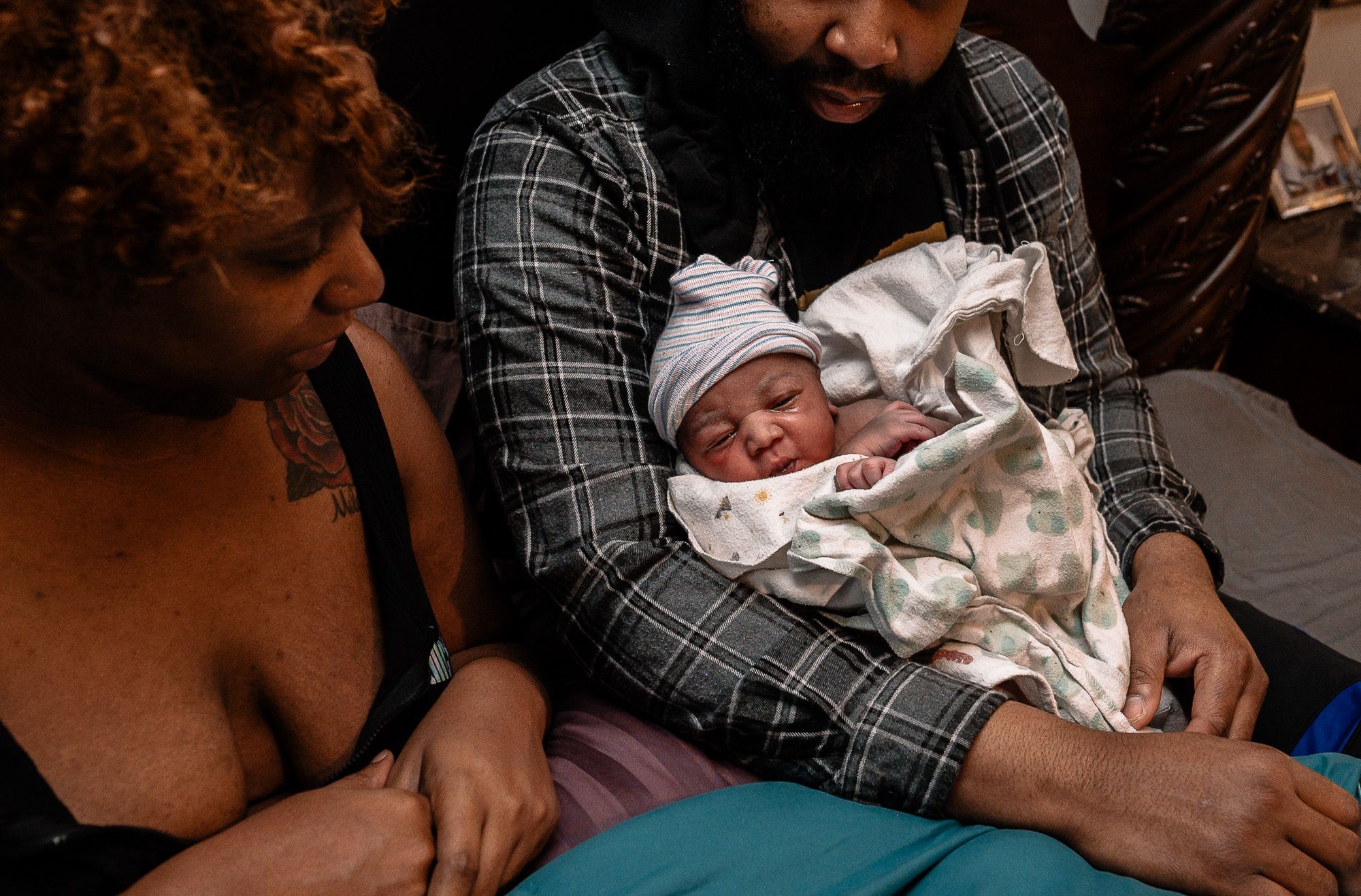 Black mother sitting next to black father holding new baby after fast birth at home