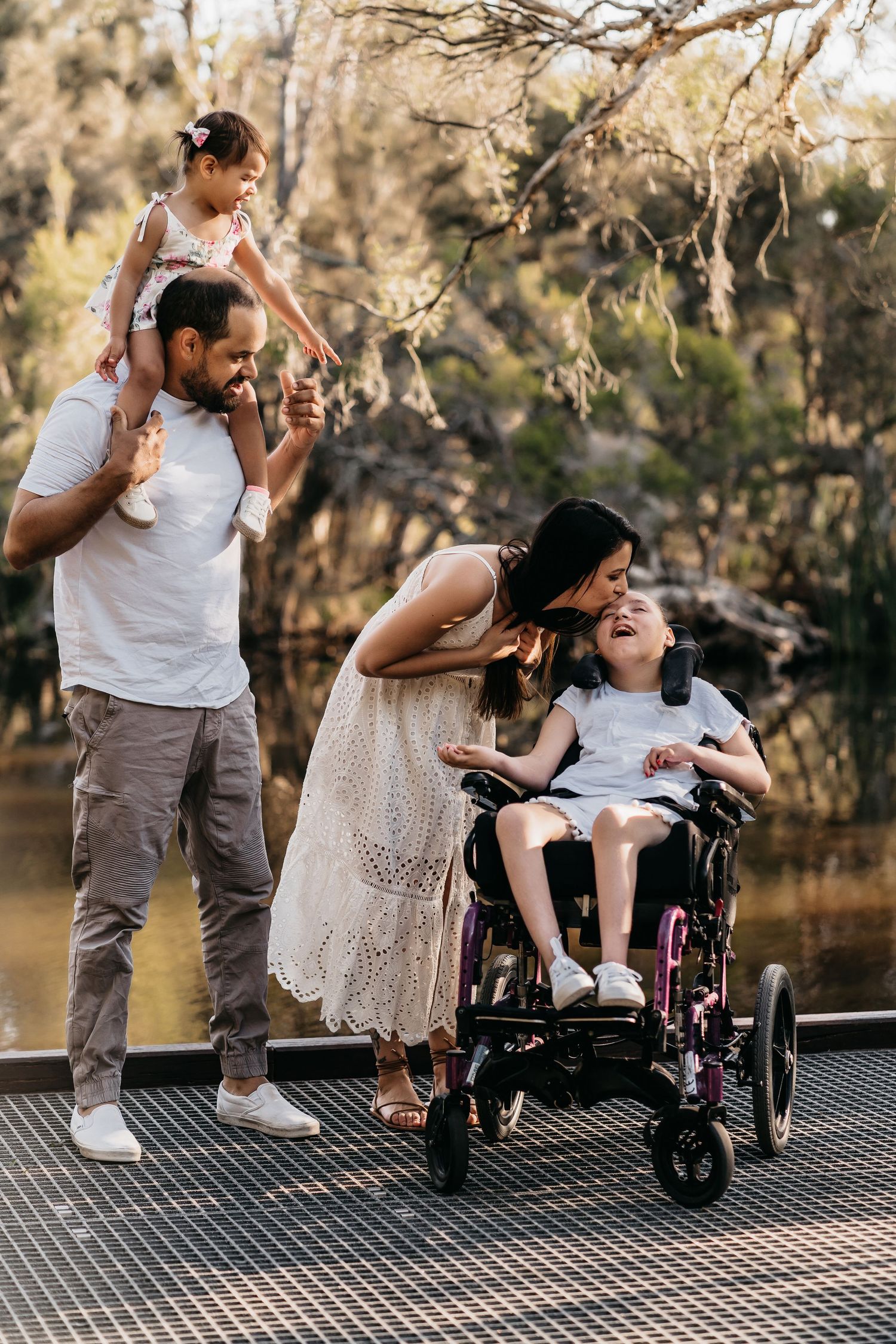 A heartwarming family moment on a wooden deck by a pond with children and wheelchair.