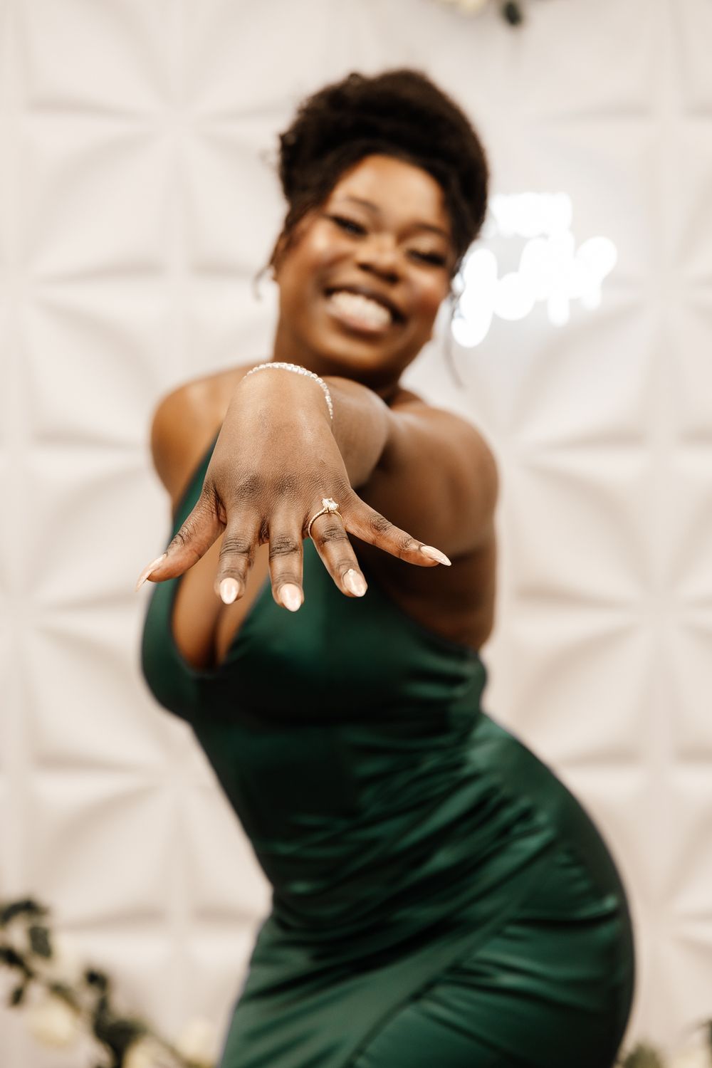 Person in emerald green dress showing off engagement ring with joyful expression.