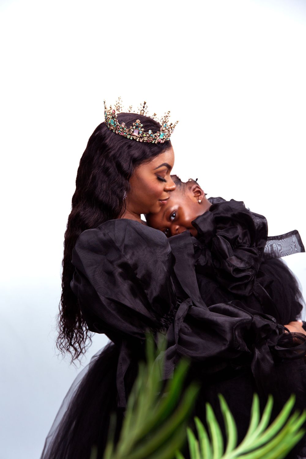 A tender moment captured in black attire with a decorative crown against a light background with palm fronds.