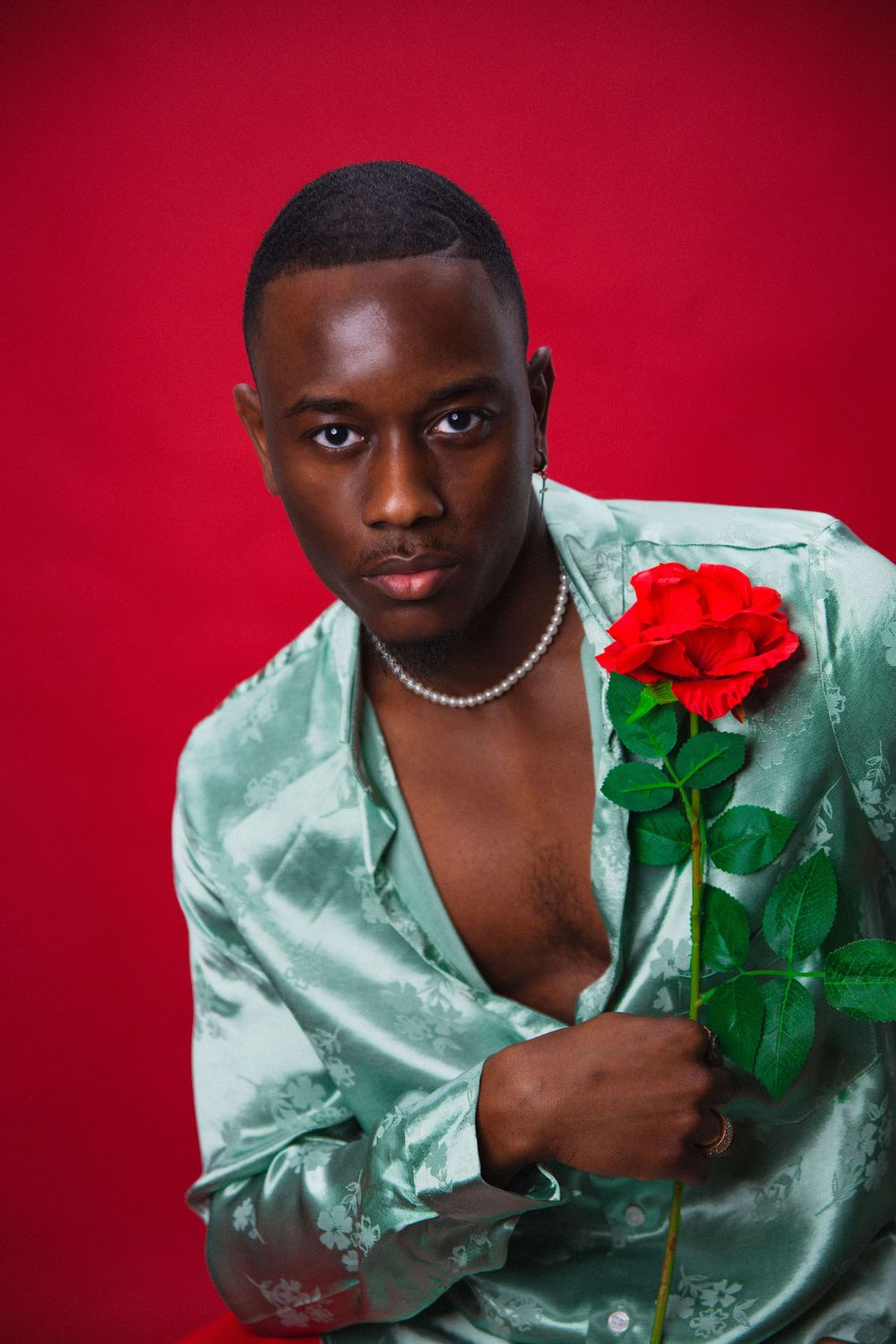Artistic portrait with a red rose against a red background featuring a mint silk shirt and pearl necklace.