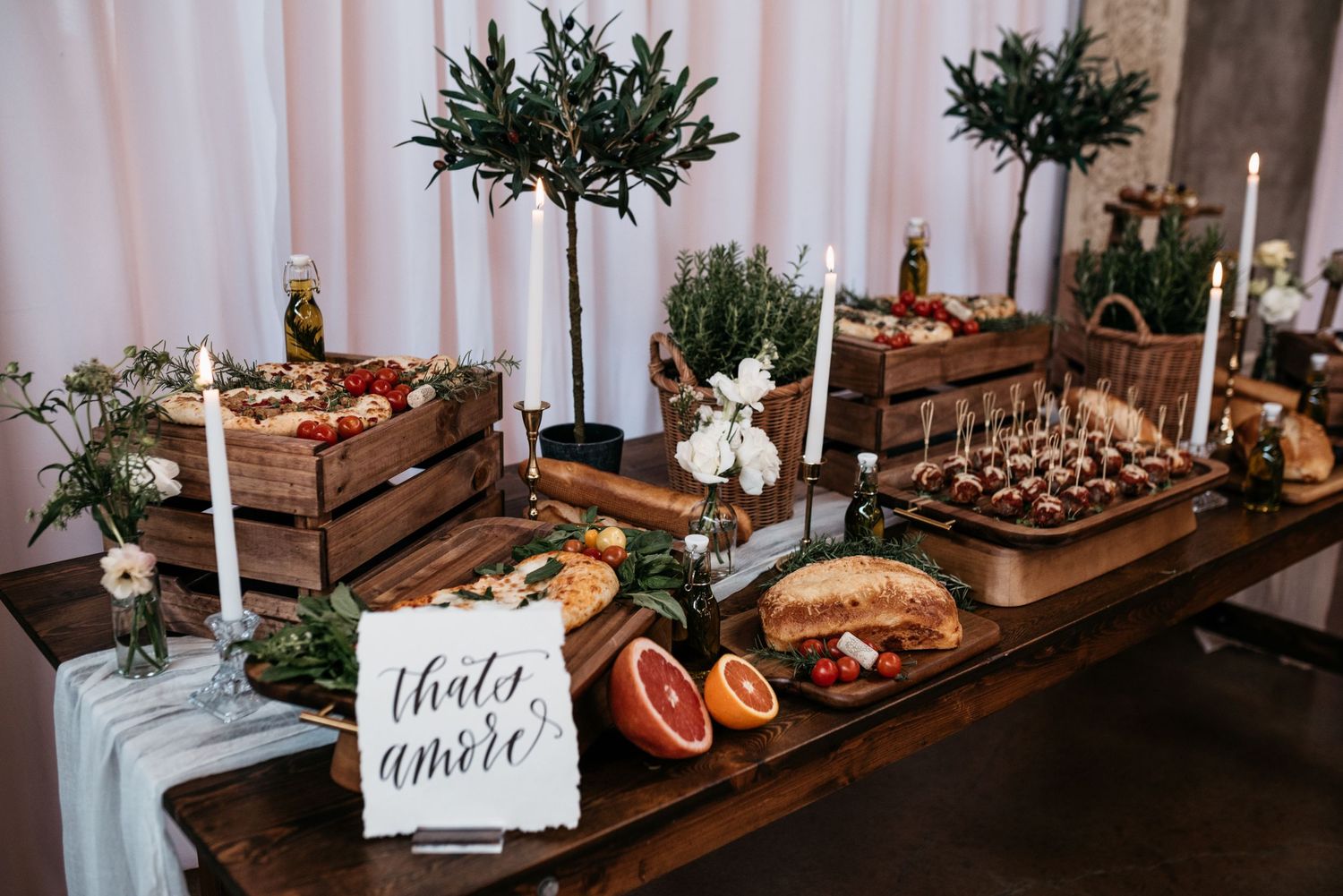 Rustic wedding buffet display with wooden crates, fresh fruit and appetizers on long table.