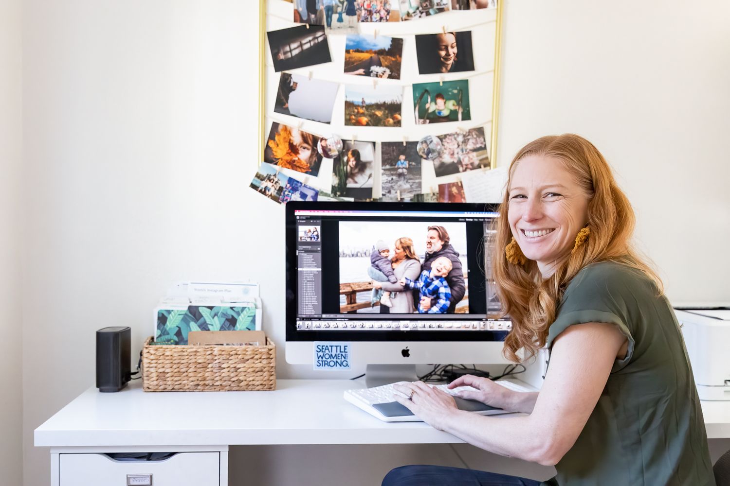 Home office setup with photo collage wall and computer screen displaying virtual meeting.