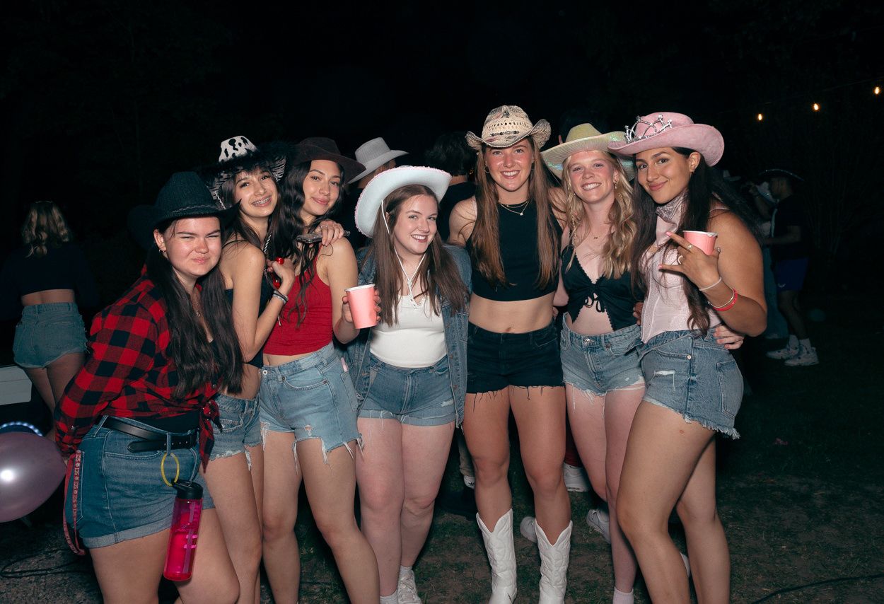 Group wearing cowboy hats and denim shorts poses together at a western-themed party.